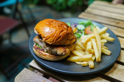 Savory grilled chicken burger and fries on wooden table close up