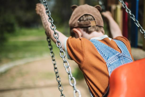 Little boy swinging at a playground in summer park stock photo