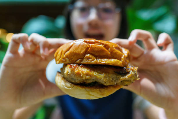 In the close-up shot, a young girl is seen enjoying a crispy chicken burger in a restaurant.