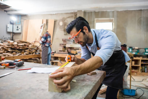 istock young carpenter caucasian man using measuring tape looking wood size at workspace. craftsman profession in wood factory. 2080682986
