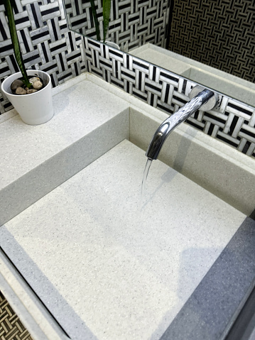 Stock photo showing close-up, elevated view of public toilet washroom with ceramic rectangular tray sink inset in counter with infrared sensor monobloc tap in front of wall mirror.