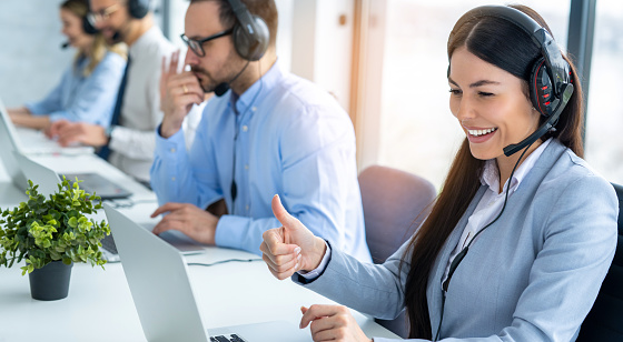 Woman customer service agent showing thumbs up to computer screen while talking online on video call with customer at call center office