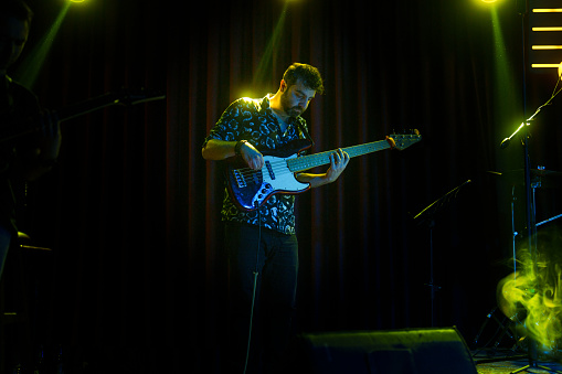 Male singer with microphone and rock and roll band performing hard rock music on stage