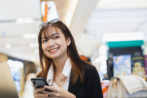 Happy smiling beautiful young asian woman using smartphone sitting at cafe. Working lady relax positive expression cheerful. Female black suit chatting on mobile phone.