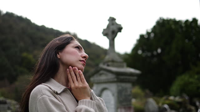 Beautiful young woman praying and mourning by tombstone at graveyard, View of Glendalough ruins in Wicklow Ireland, view of Glendalough abbey, view of Glendalough upper and lower lakes in Ireland, popular tourist destination in Ireland