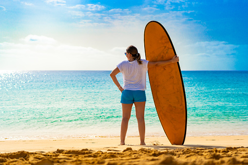 Beautiful woman holding surfboard standing on sunny beach Santa Maria, Sal island , Cape Verde