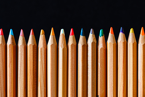 Color image depicting a close up macro view of a collection of colored pencils in a row, on a black background.
