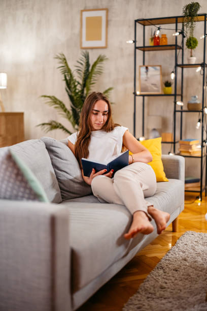 istock Young Woman Sitting On The Sofa And Reading A Book 2080754693