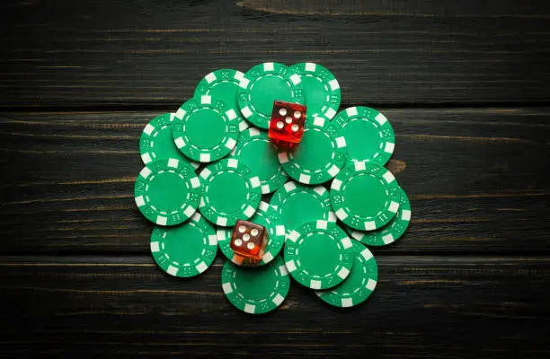 Photo of Green chips on a vintage dark table from a successful combination in a game of dice or craps. Low key concept of a gambling and popular game