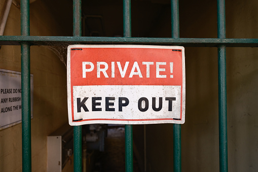 Metal privacy sign on a green gate with dark passage beyond.