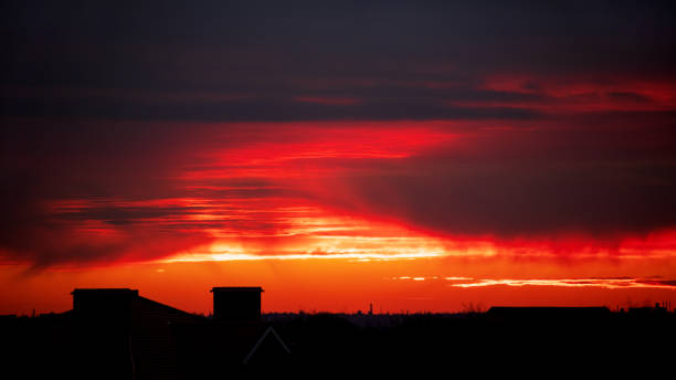 Hermosa vista del cielo rojo con cirros durante la puesta de sol. Techos de casas bajo los rayos del atardecer. Fondo texturizado de una hermosa puesta de sol. - foto de stock