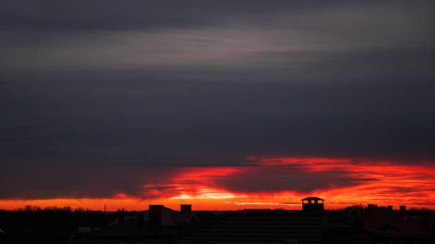 Beautiful view of the red sky with cirrus clouds during sunset. Roofs of houses in the rays of sunset. Textured background of a beautiful sunset. - foto de stock