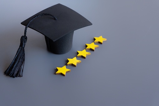 Graduation cap next to a row of five stars rating on a gray background. Copy space for text. Best education system concept.