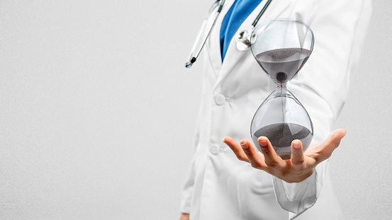 Woman in doctor suit holding an hourglass isolated on white background. Deadline concept.