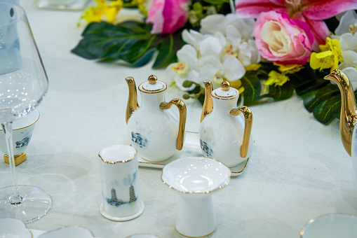 Set of vintage ceramic factorycrafted tableware with flowers of subtle colors on white tablecloth, 11 pieces, top view