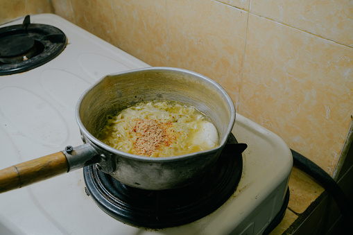 Noodles and boiled eggs cooked in hot water using a stove.\nProcess of cooking boiled noodles with egg.