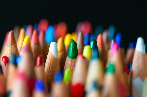 Color image depicting a close up macro view of a collection of colored pencils, on a black background. Selective focus image with one of the pencils in sharp focus with the others blurred out of focus.