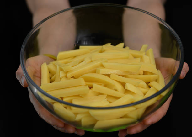 un tazón de papas amarillas crudas cortadas en palitos para papas fritas sostenidas en las manos - french fries fast food french fries raw raw potato fotografías e imágenes de stock