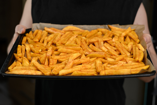 Homemade fries, a man holds a baking tray filled with sliced ​​potatoes