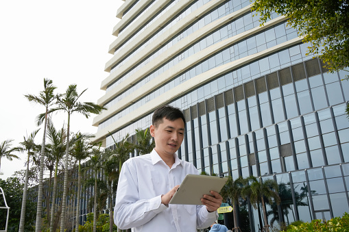 A man uses a tablet computer in front of a hotel on vacation
