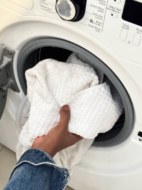 istock Close-up image of front loading, washing machine with open door, dirty white towels being placed into machine drum by unrecognisable person, elevated view, focus on foreground 2080974627