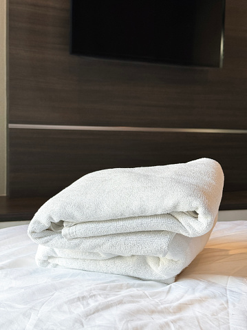 Stock photo showing close-up view of pile of folded, white towels sitting on hotel room duvet bedding.