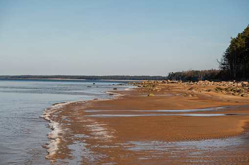 A serene beach with gentle waves lapping against the sandy shore under a clear blue sky.