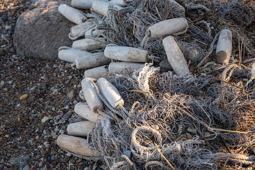 Discarded fishing net and plastic bottles polluting a rocky beach.