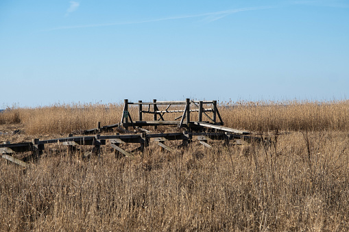 An abandoned, decayed wooden structure in a vast, dry grass field under a clear sky.
