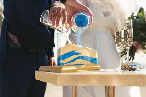 The newlyweds together pour white and blue sand into a vase.