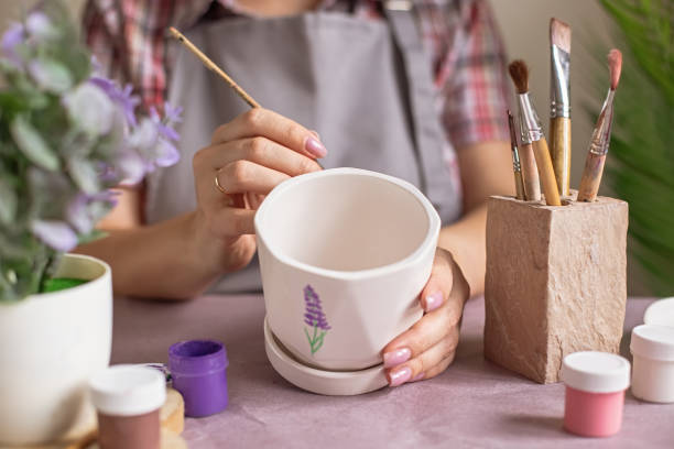 istock Women in gray apron paint a white flower ceramic pot on the table 2080996331