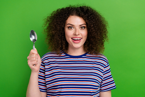 Portrait of positive astonished hungry girl beaming smile arm hold spoon isolated on green color background.