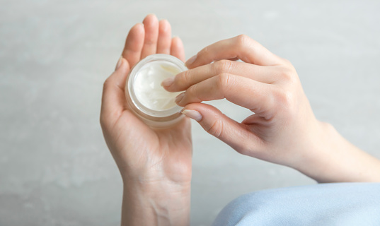 A jar of cream in the hands of a woman, top view. A woman holds hand cream in her hands