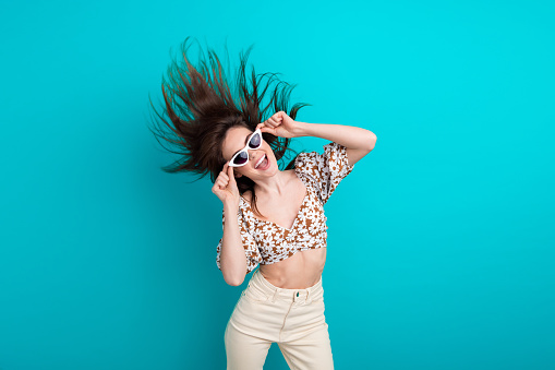 Photo of girlfriend young fashionista touching her gucci sunglasses shaking head flying hair and dance isolated on cyan color background.