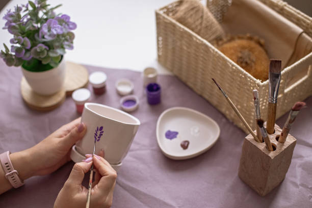 istock Womens hands paint a white flower ceramic pot on the table 2081067347