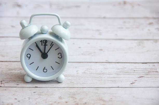 White alarm clock pointing at 11am on wooden table. Copy space and time concept.