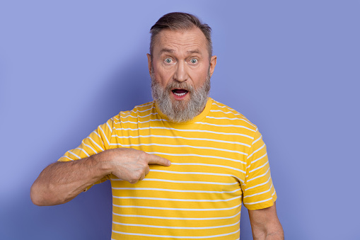 Photo of stunned pensioner man dressed striped t-shirt indicating at himself astonished staring isolated on purple color background.