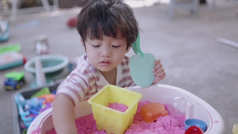 Happy Asian boy play with pink science sand on the toy tray at home.