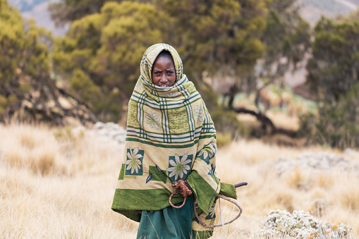 Simien Mountain, Ethiopia - April 25, 2019: A young Ethiopian shepherdess girl, wrapped in a blanket on a cold morning. Daily life of ordinary highlanders in Simien Mountains.