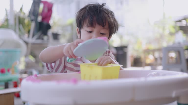 Happy Asian boy play with pink science sand on the toy tray at home.