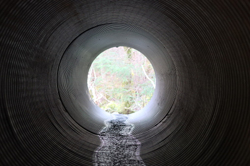 View through a round tunnel carrying a stream beneath a road
