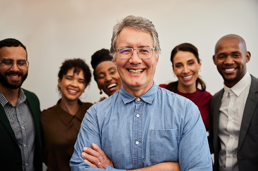 Portrait of a mature businessman smiling with a group of diverse colleagues standing behind him in front of a white office wall