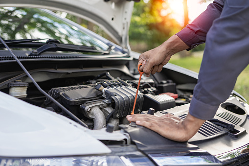 Auto mechanic looks under the hood of a broken car and checks the oil level on the side of the road. Car broken down on the side of the road, man trying to repair broken old car, car service concept