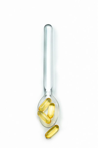 Capsules pills on a  glass spoon, isolated on white, high angle view. Studio shot.