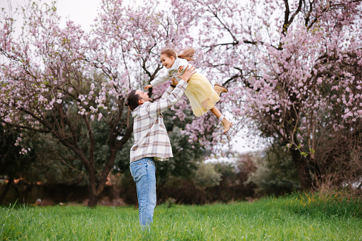 Happy young father and daughter having fun while running in spring day at the park. Blooming trees