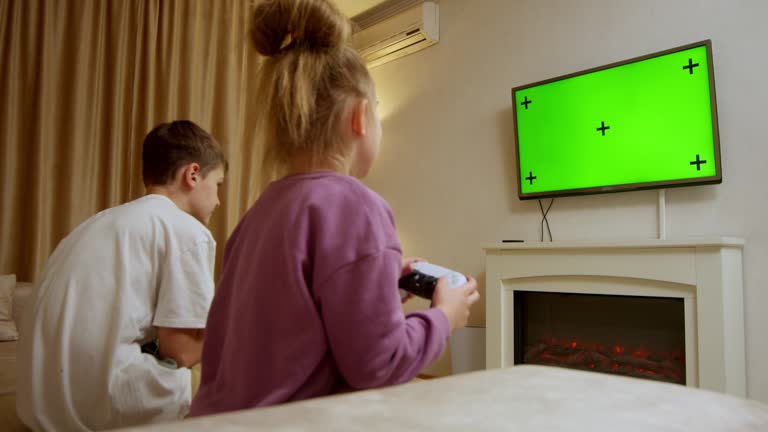 Children in a home interior enjoying playing a game console against a green TV screen background. Game console, video games, technology, recreation.