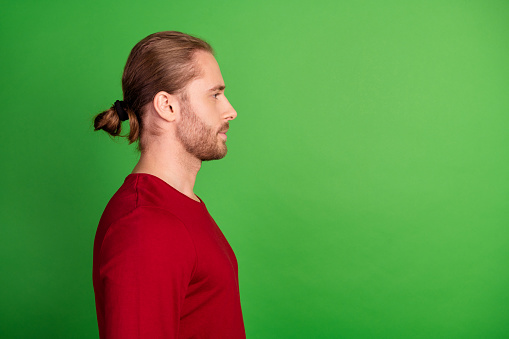 Side profile photo of virile guy with man bun wear red sweatshirt look at barbershop ad empty space isolated on green color background.
