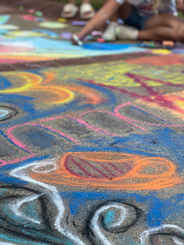 The sidewalk of a public park is covered with colorful chalk art at a locak chalk art festival.