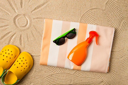 drawing on the sand, sun and waves,sunglasses, with an orange bottle, yellow rubber slippers, beach towel, sun spray,on the sand, top view, no people,