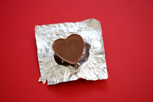 chocolate candy in the shape of a heart in a silver package on a red background. chocolate candy closeup on a red background. red background